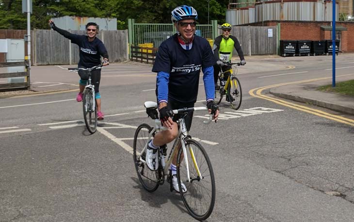 3 people dressed in bike riding gear waving to the camera.